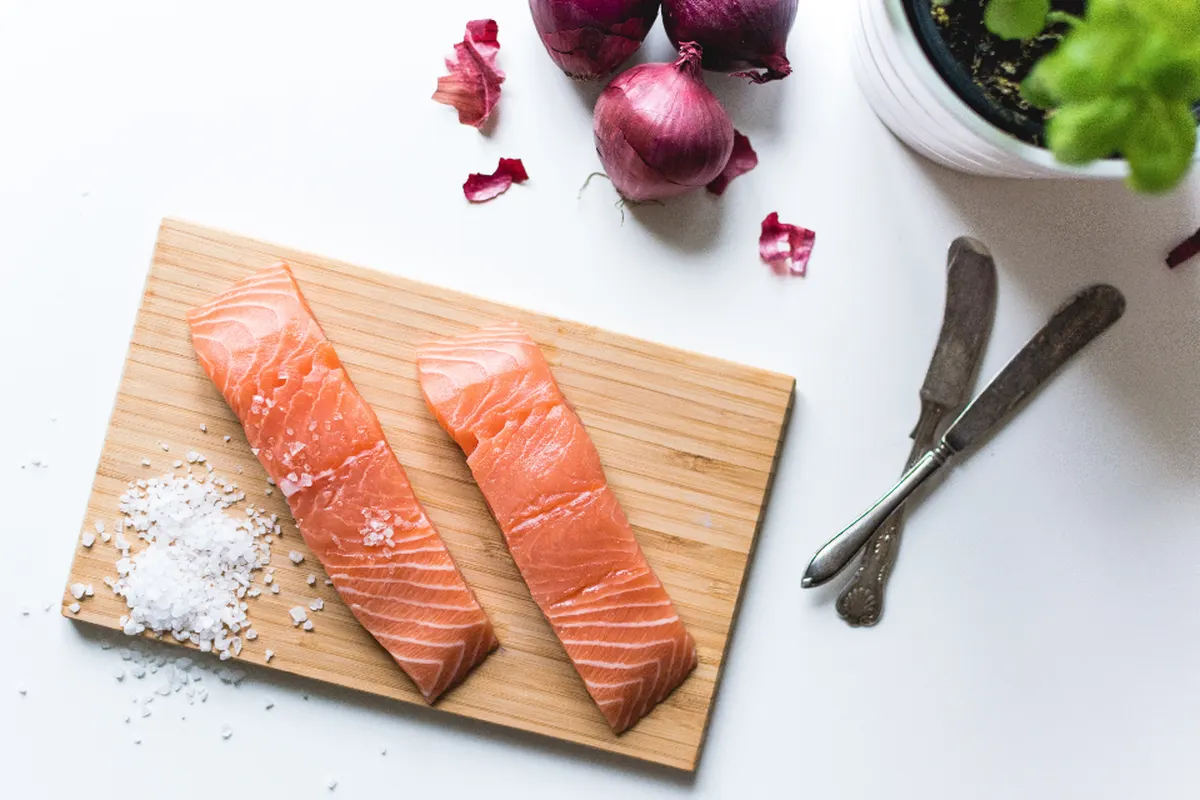raw salmon fillets on a board with herbs