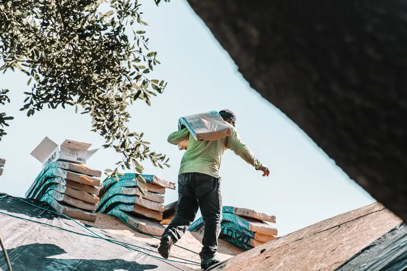 roofer carrying a bundle of shingles across a roof