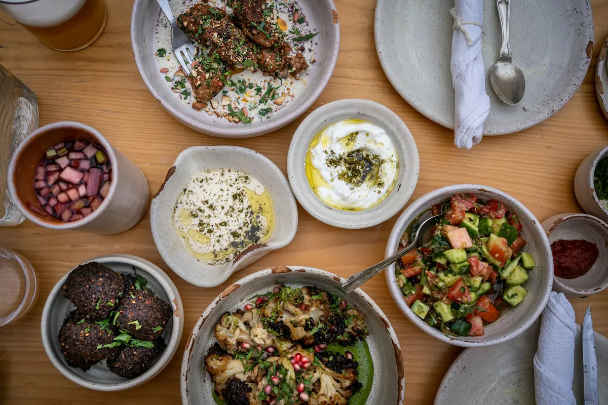 overhead view of a table spread with hummus, salads, grilled vegetables, and small shared plates