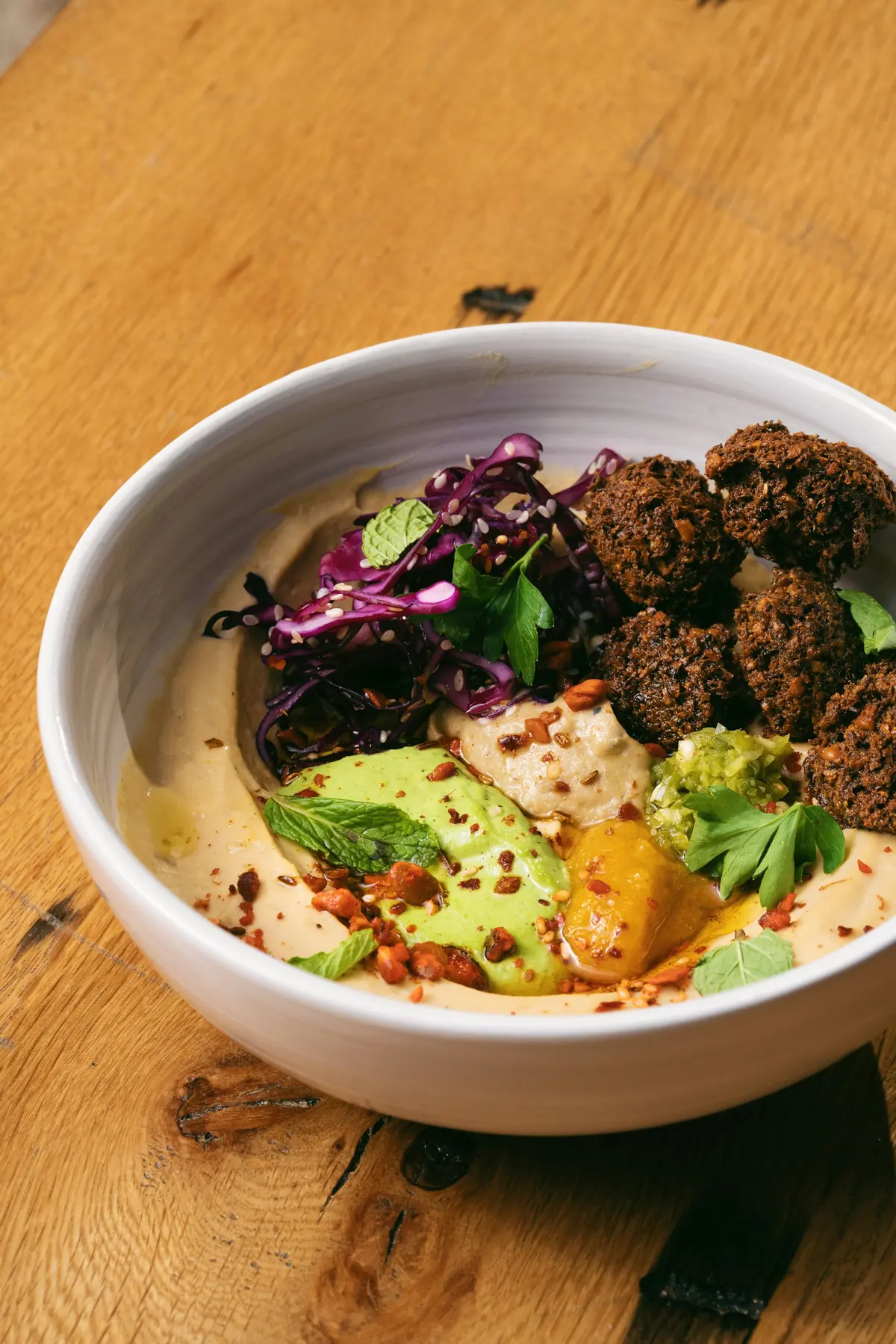 falafel bowl with hummus, red cabbage, and fresh herbs on a wooden table