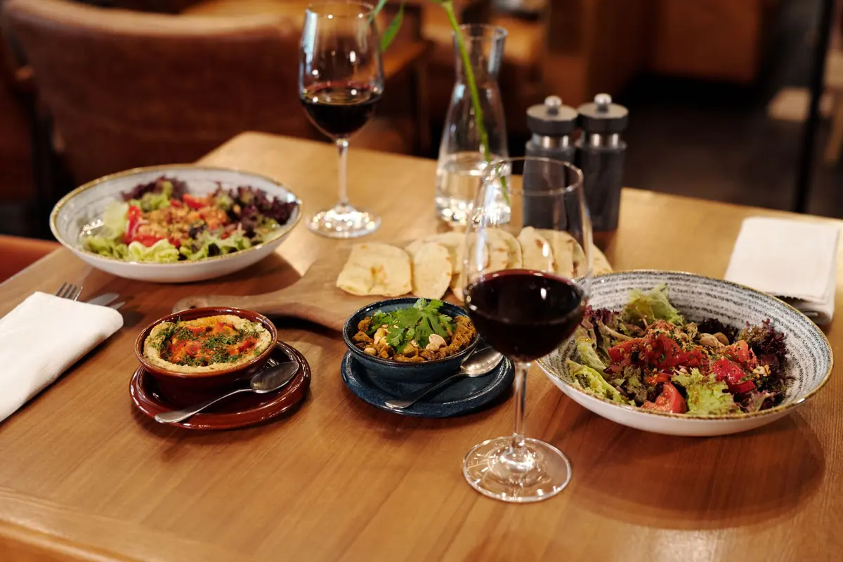table set with small plates, salads, and glasses of red wine