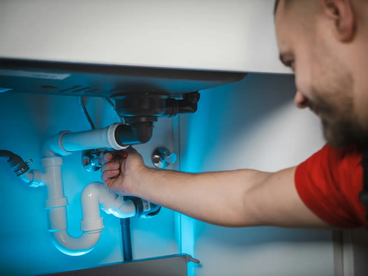 Riverline plumber repairing pipes under a sink by flashlight