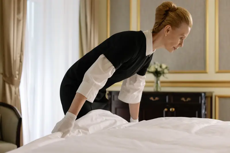housekeeper in a black uniform smoothing crisp white bed linen
