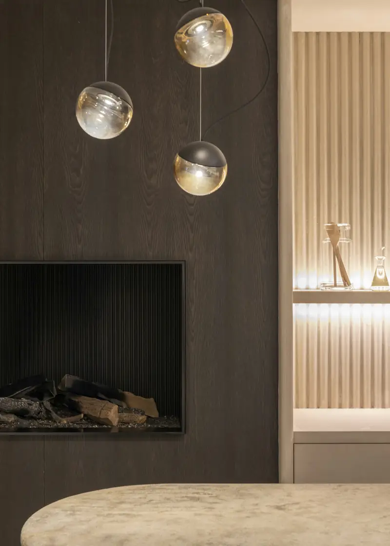 glass pendant lights over a stone counter beside a dark fireplace wall