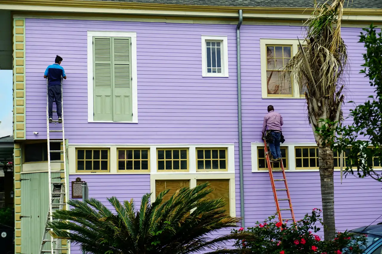 two Delgado & Sons painters on ladders repainting a lavender clapboard house framed by palms
