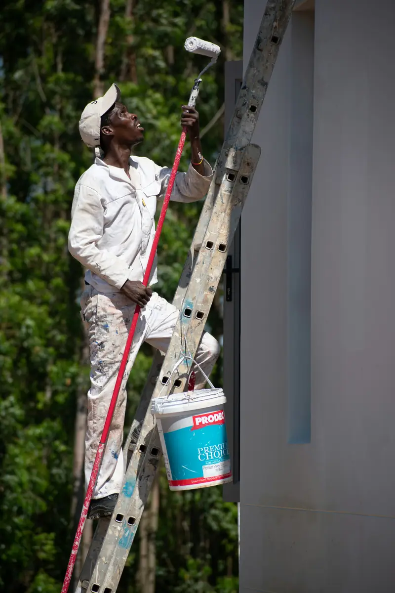 Andre Baptiste on a ladder painting a two-story wall