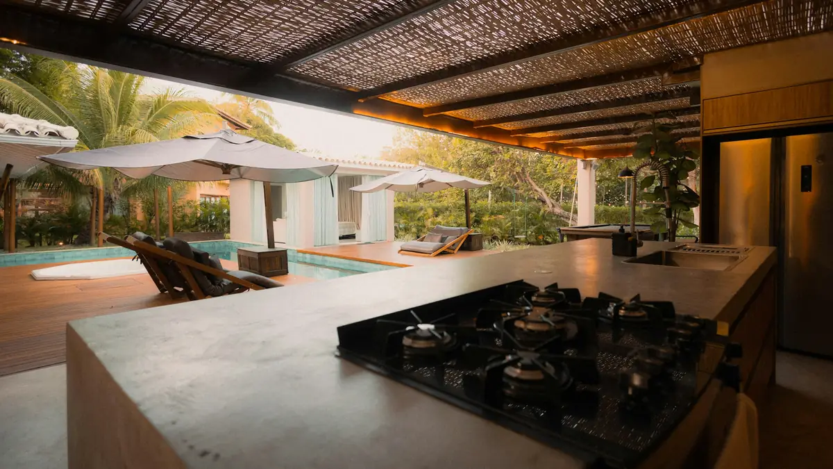 outdoor kitchen island with gas cooktop overlooking a pool under a shade roof