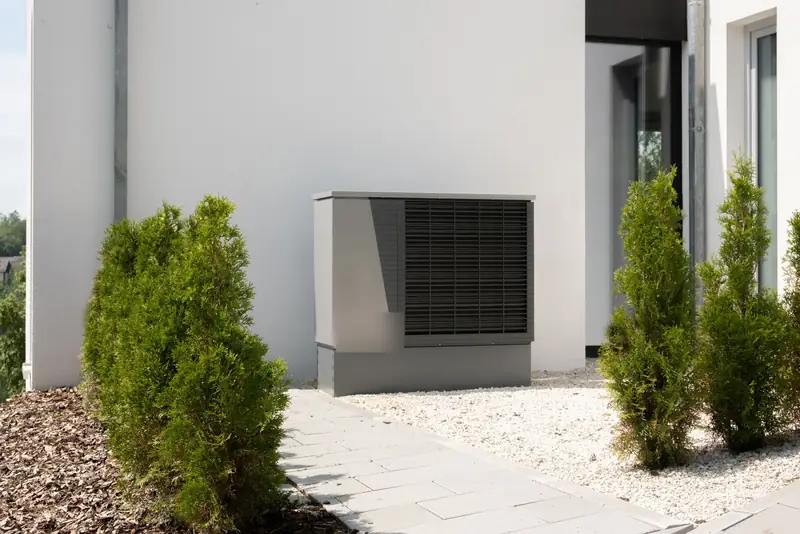 new outdoor AC condenser installed on a gravel pad beside a white home